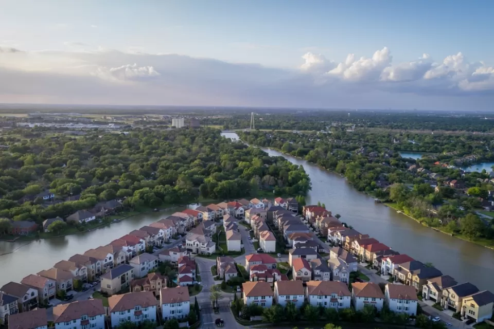 Aerial view of neighborhood with homes along a bayou surrounded by green trees in Sugar Land, Texas